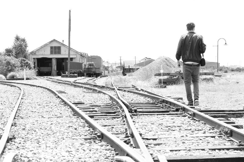 Man on railroad tracks against clear sky