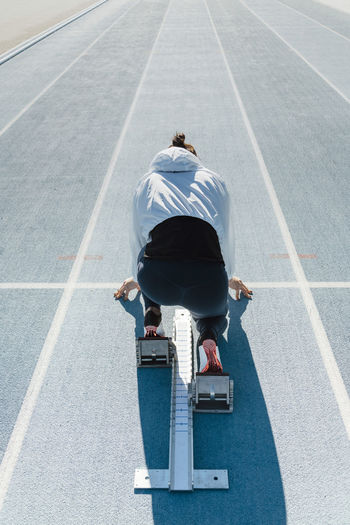 Back view of unrecognizable sportswoman in sportswear beginning race from crouch start position on starting blocks in a sunny day on stadium