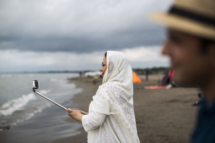 Side view of woman taking selfie while standing on beach