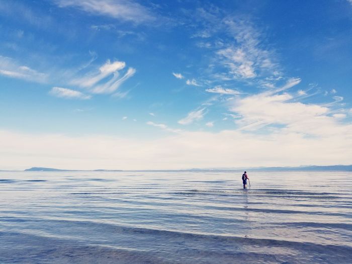 Man standing in sea against blue sky
