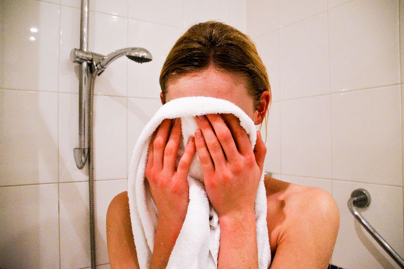 Close-up of woman rubbing towel on face while standing in bathroom