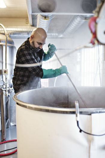 Male worker stirring beer in container while working at brewery