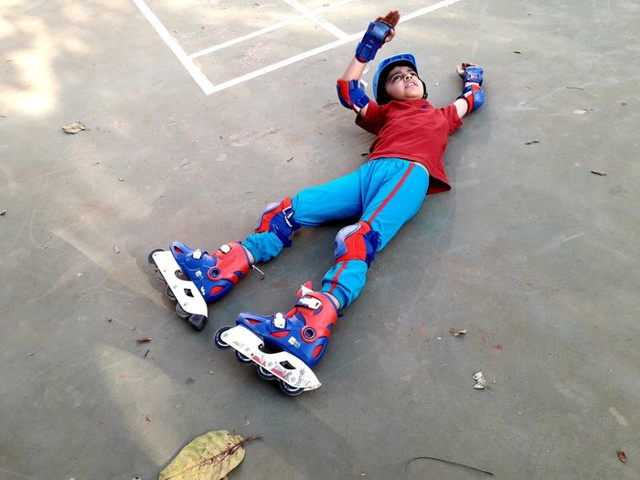 High angle view of fallen boy with inline skates lying on playground