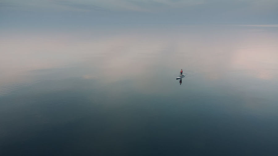 A woman is sailing on a sup board on the mirror surface of the sea. alone with the natural element