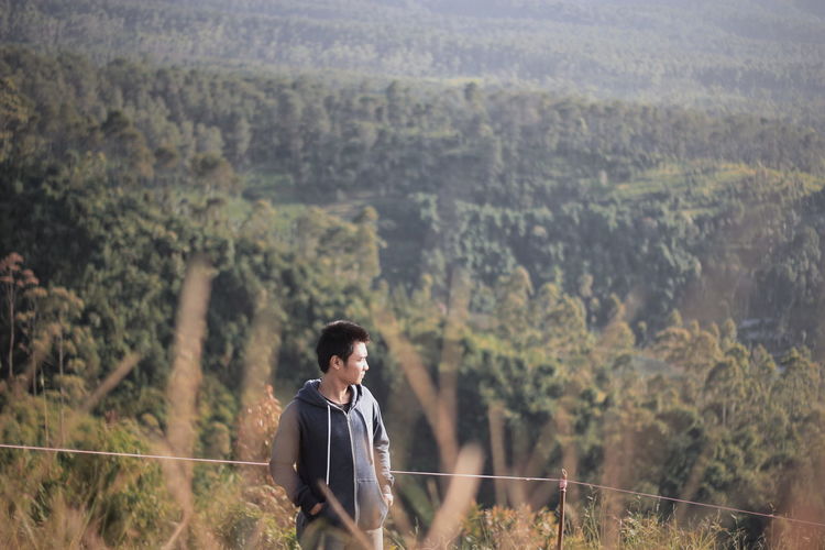 Young man standing on field against trees