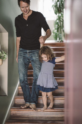 Father holding hands with daughter while climbing steps at home