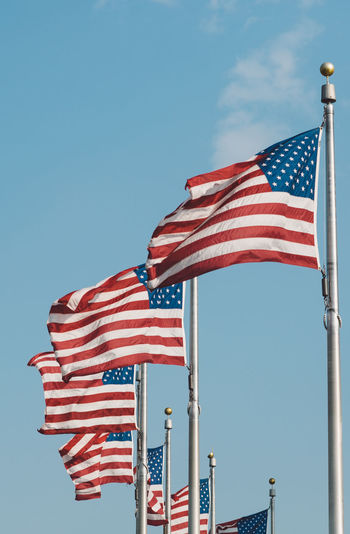 Low angle view of american flags fluttering against blue sky