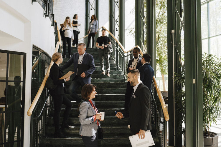 Male and female colleagues discussing together while standing at staircase during networking event