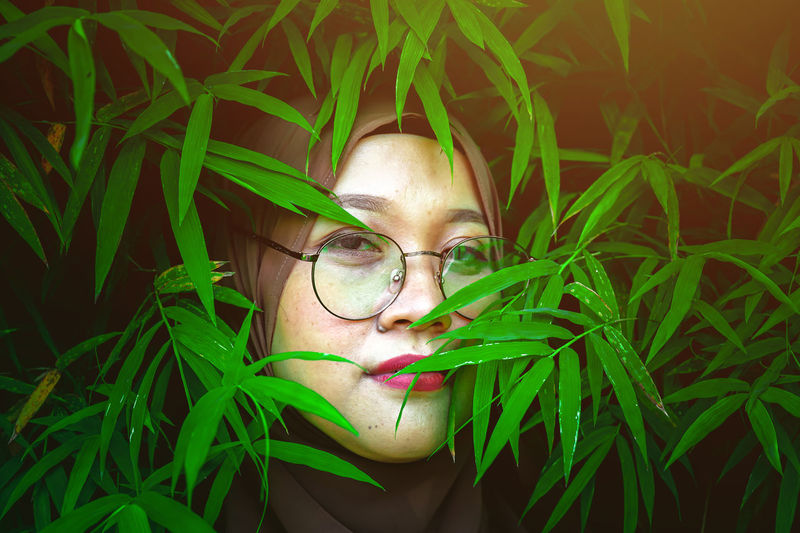Close-up portrait of young woman with eyeglasses on plant