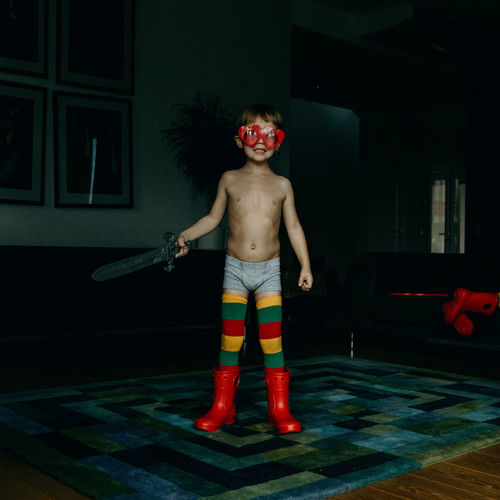 Full length of shirtless boy playing with sword toy at home