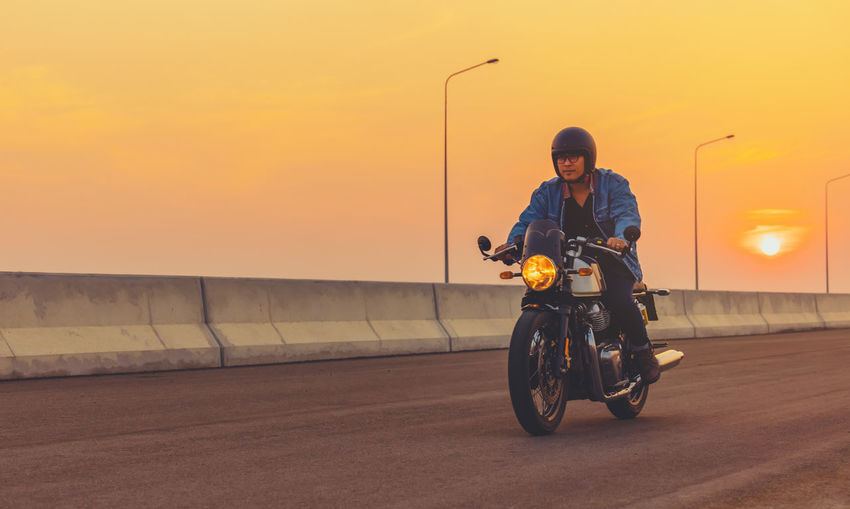 Young man riding big bike motocycle on asphalt high way against at sunset