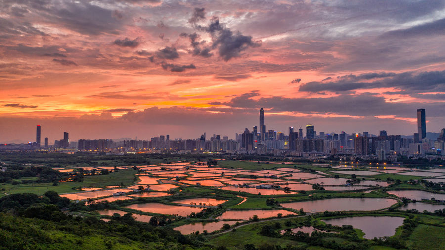Landscape and cityscape against cloudy sky during sunset