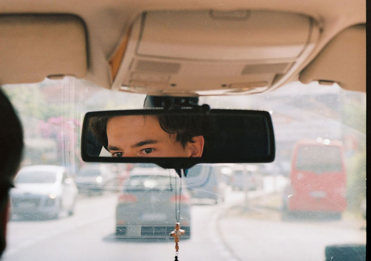 Eyes of a young man in the rear-view mirror of a car
