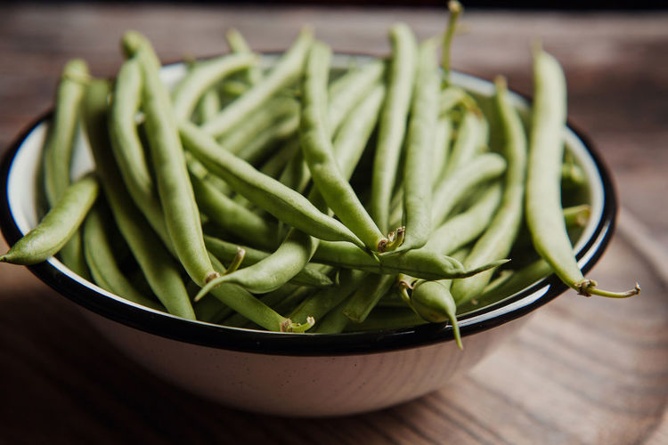 Top view of fresh whole and cut green beans in wooden and metal bowls on linen towel
