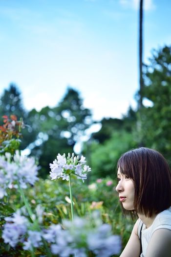 Woman standing by flowering plants against sky