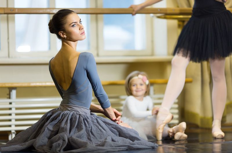 A little ballerina ties pointe shoes to an adult ballerina.