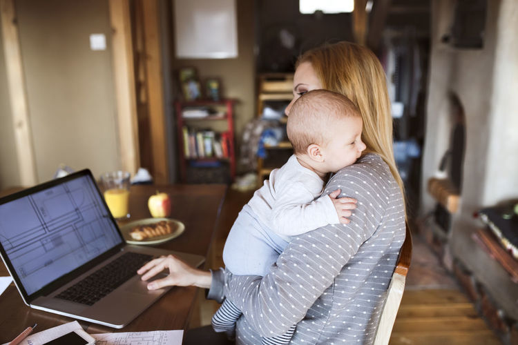 Mother with baby at home using laptop