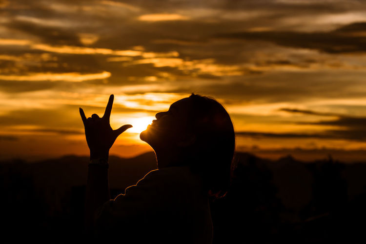 Silhouette woman gesturing against orange sky