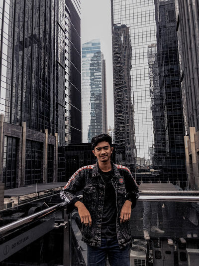 Portrait of young man standing against buildings in city