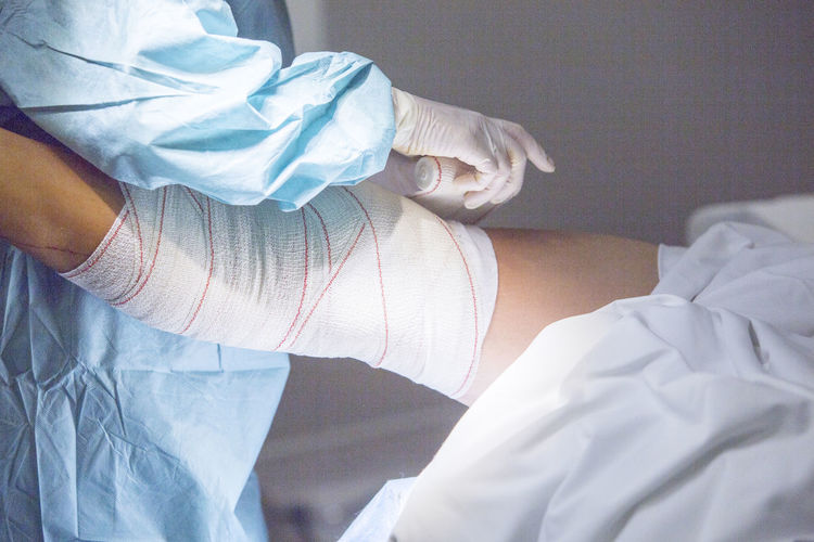 Midsection of doctor wrapping adhesive bandage on patient leg in hospital