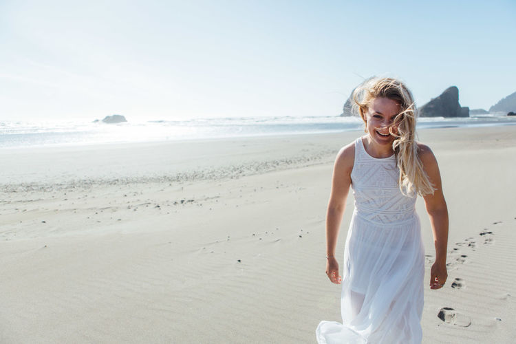Portrait of smiling young woman standing on beach against clear sky