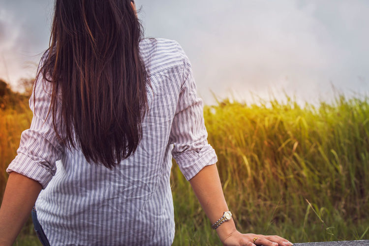Rear view of woman sitting on field against sky