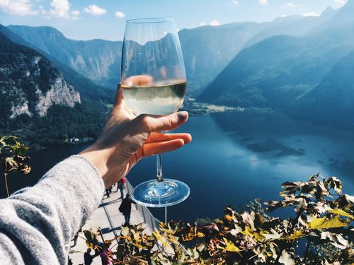 Close-up of human hand holding alcoholic drink by lake against mountains