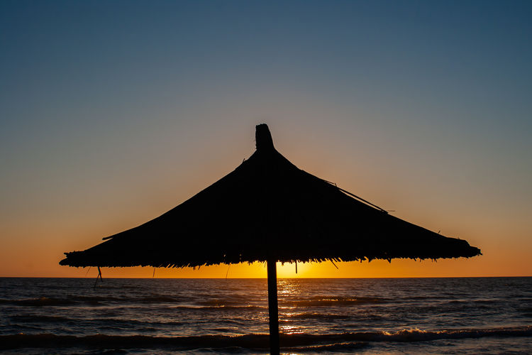 Silhouette built structure on beach against clear sky during sunset