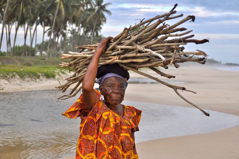 Portrait of senior woman with stack of logs on head at beach