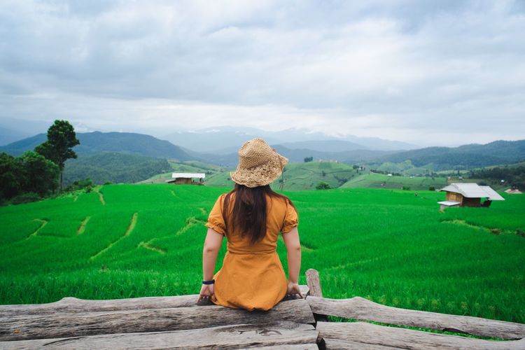Rear view of woman wearing hat looking at landscape against sky
