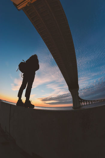 Silhouette man standing by bridge against sky during sunset