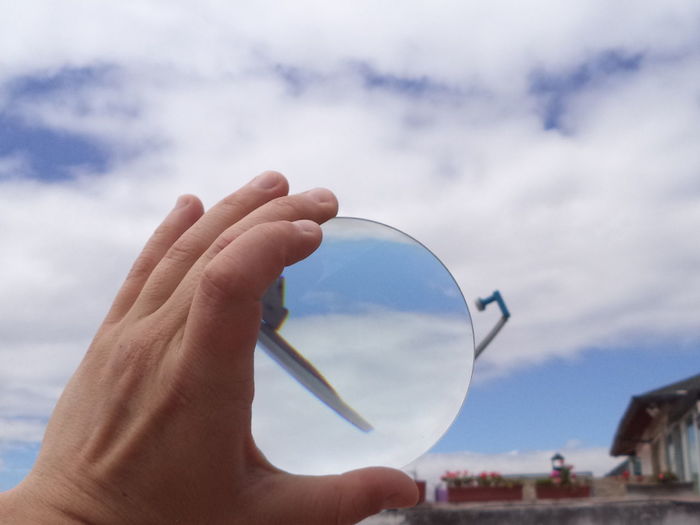 Cropped image of hand holding lens against cloudy sky