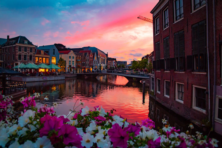 Scenic view of river by buildings against sky during sunset