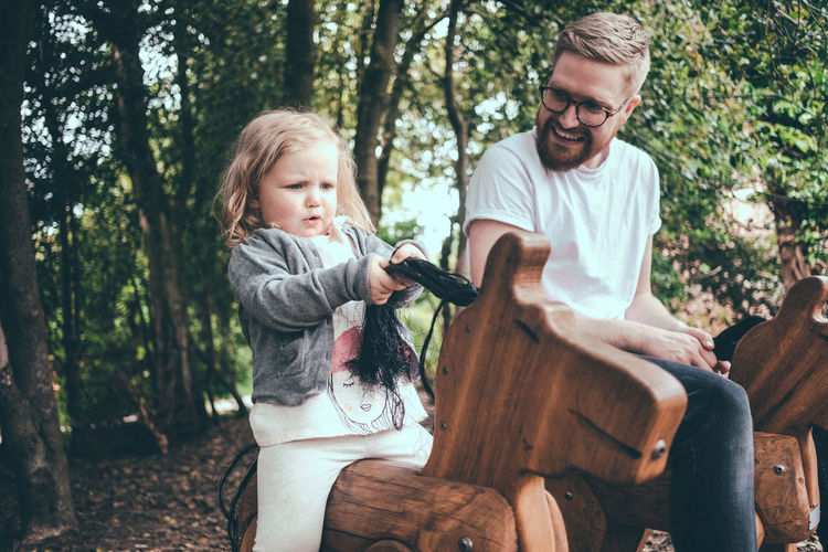 Happy father looking at daughter riding wooden horse in park