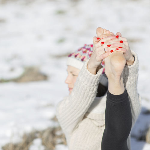 Close-up of bare foot young attractive woman practicing yoga on snowy field