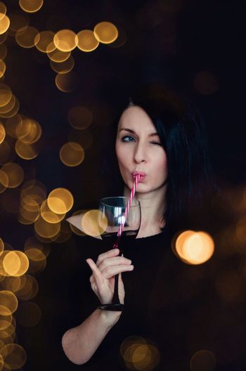 Girl with a glass of red wine and a striped straw in the lights.