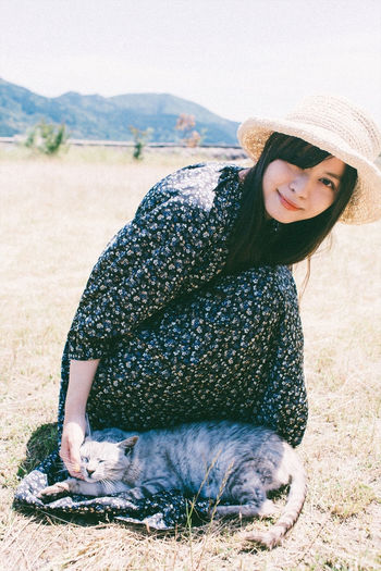 Portrait of smiling young woman sitting on field with a cat 