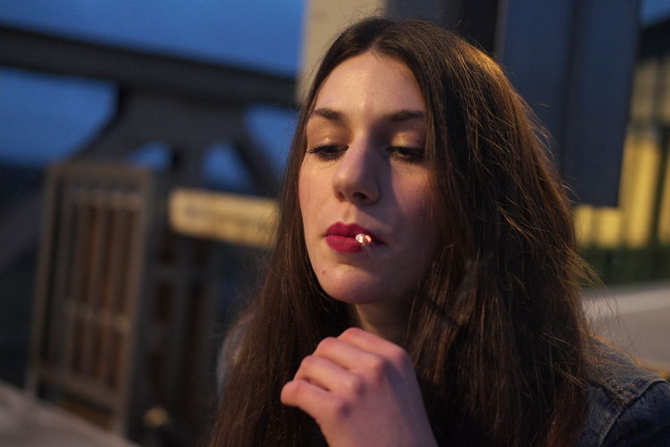 Close-up of young woman smoking cigarette in city at night