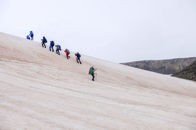 People walking on snowy mountain against clear sky
