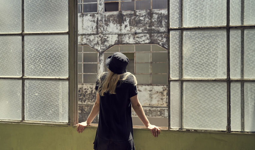 Rear view of woman in black dress standing with blonde hair against old window