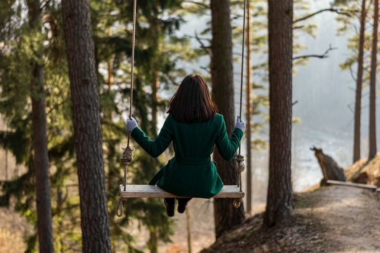 Rear view of woman sitting on swing in forest
