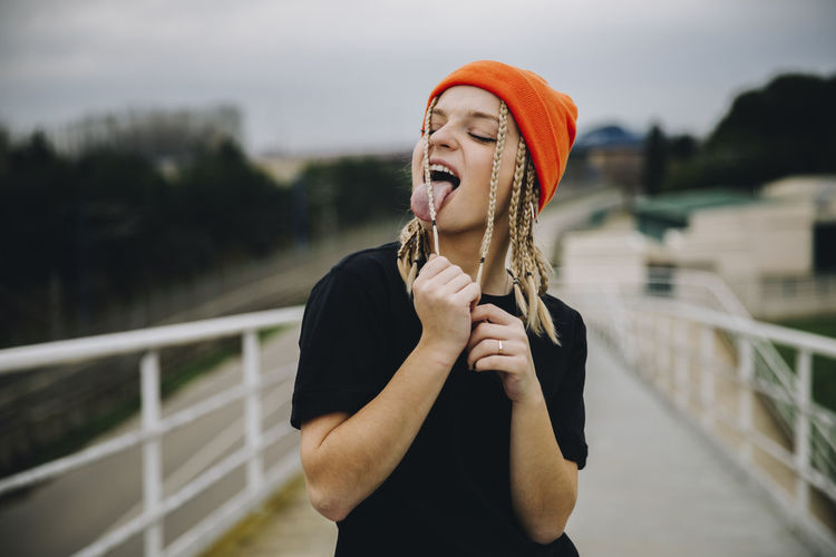 Young woman licking braided hair while standing on footbridge
