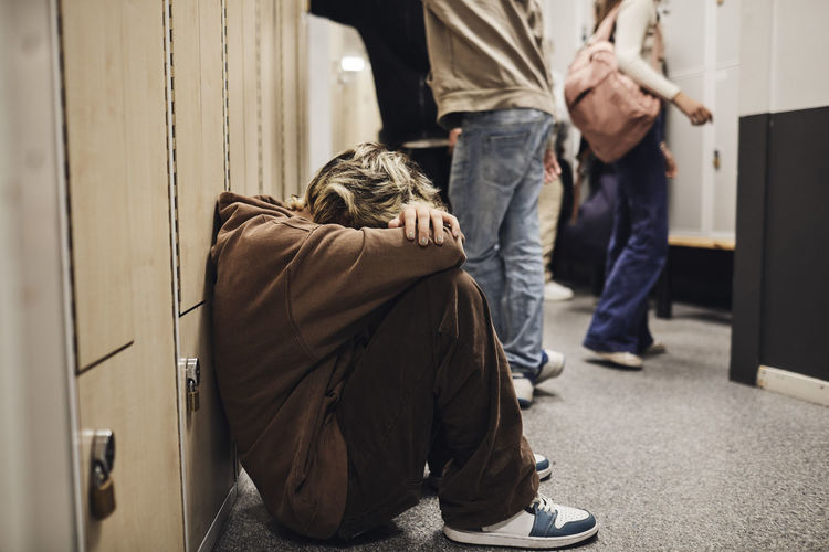 Full length of sad teenage girl sitting in school corridor
