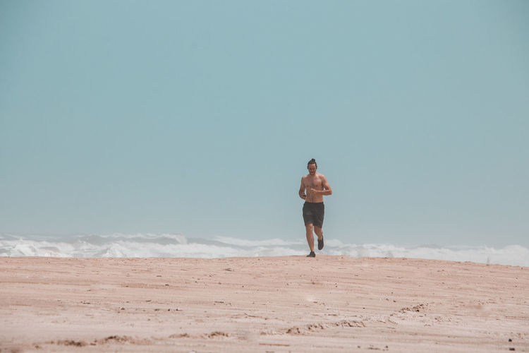Shirtless man running at beach against sky