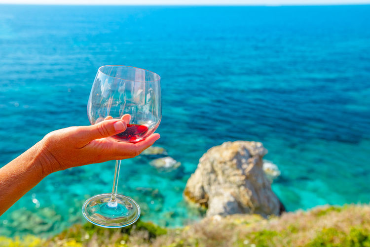 Close-up of hand holding glass against sea