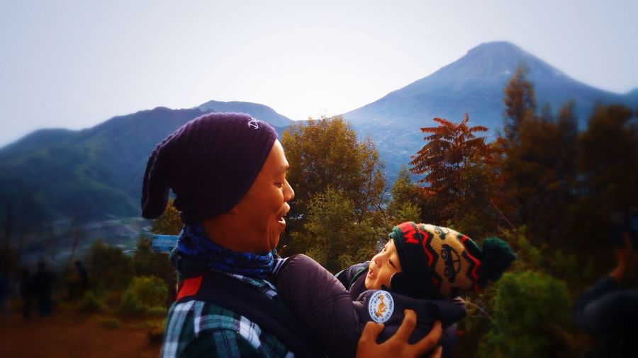 Smiling father with boy standing against tree and mountain