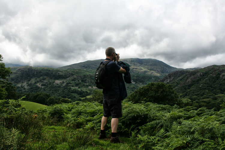 Rear view of man standing on mountain against distant mountains and sky in peak district, england