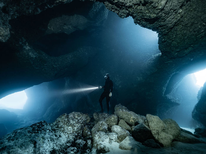 People swimming in sea freediving underwater cave with a torch