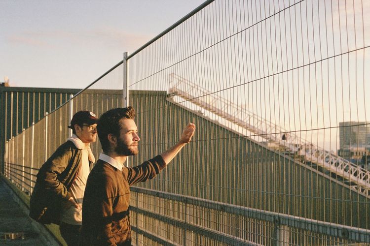 Men standing on railing by fence