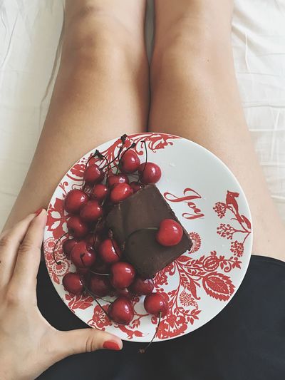 Midsection of woman holding chocolate cake with cherries in plate on bed